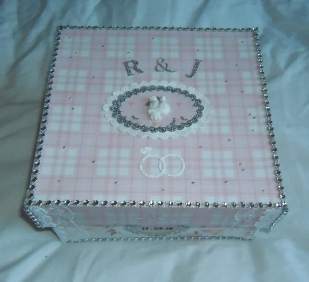 Wedding#4 photo album box is covered in a charming pink and white chequered paper. At the centre, there's an oval pink cut-out surrounded by a silver frame. Inside the pink oval, a pair of white turtle doves are featured