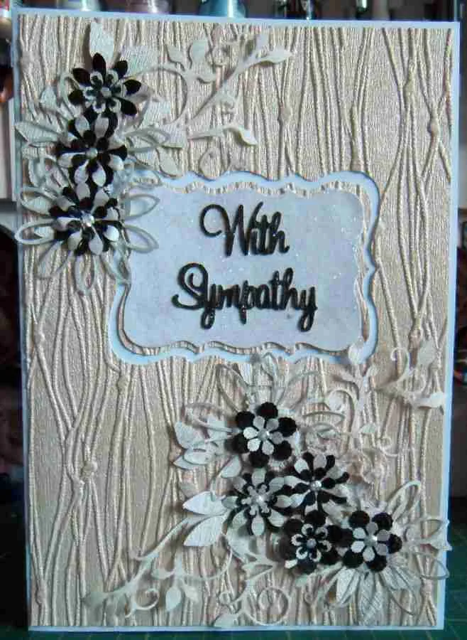 Sympathy Card-1 A cream-textured sympathy card with black and white flower embellishments and an ornate white rectangle in the centre, featuring the words "With Sympathy" in black script.