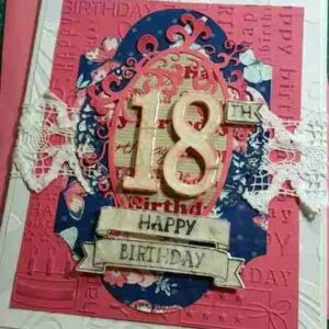 18th Birthday Card is an embossed pink background, textured white layer, and blue die-cut shape. A white lace band crosses the centre, with a peach-coloured oval frame containing a 3D number "18" and a "Happy Birthday" tag.