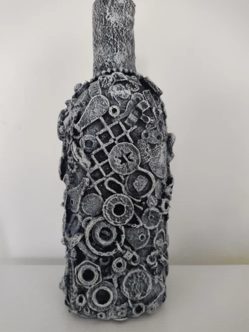 Bottle-0-Rum, right side of the mixed media bottle covered by pieces of metal, plastic and textures, the background base colour is black with highlights of white on top giving the whole bottle a greyish finish.