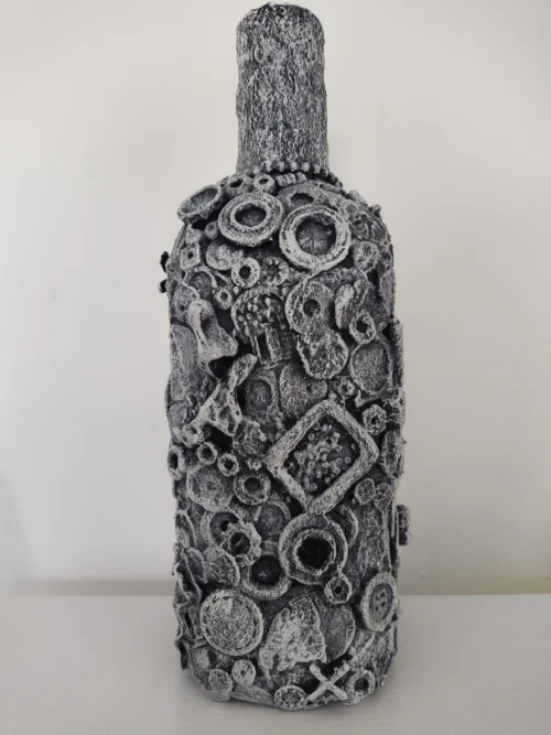 Bottle-0-Rum, back of the mixed media bottle covered by pieces of metal, plastic and textures, the background base colour is black with highlights of white on top giving the whole bottle a greyish finish.