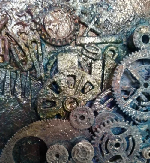 Mechanical Rainbow-1, close up section of the mixed media used on this canvas. It shows textured layers of card, plastic and metals, cogs are laid on top in layers so you can see the ones below them. A rainbow of colours cover the canvas with highlights of silver on top.