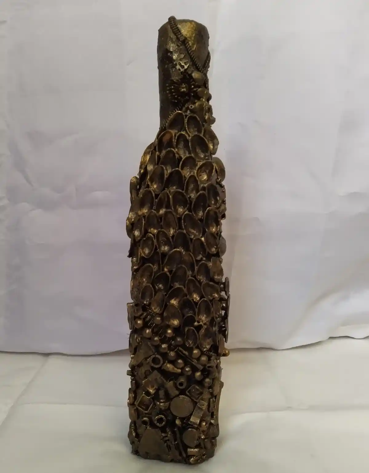 Bronze Bottle, back of the bottle is covered in recycled mixed media and nut shells, all with a golden bronze finish.