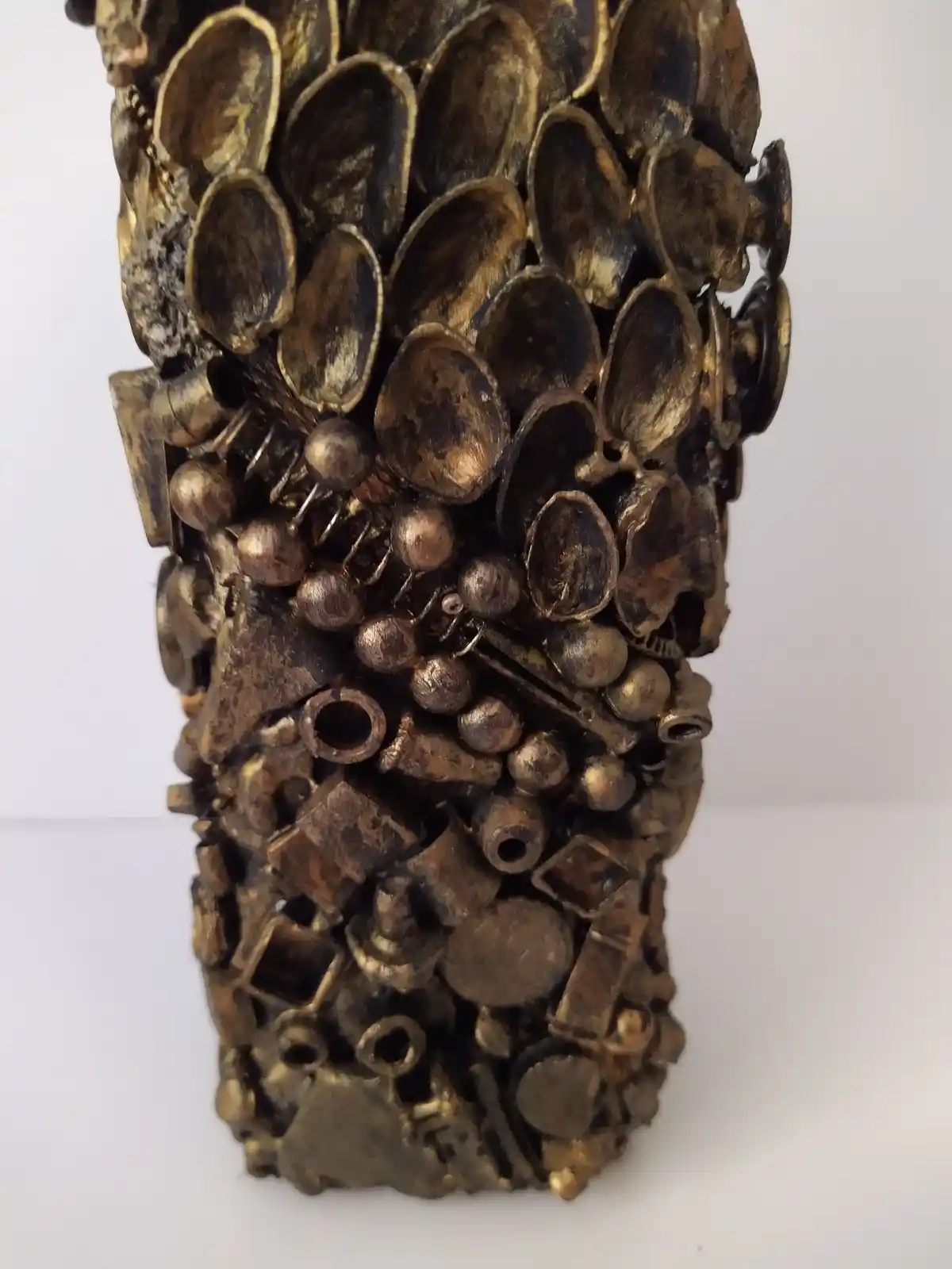 Bronze Bottle, close up shot of the back of the bottle covered in recycled mixed media and nut shells, all with a golden bronze finish.