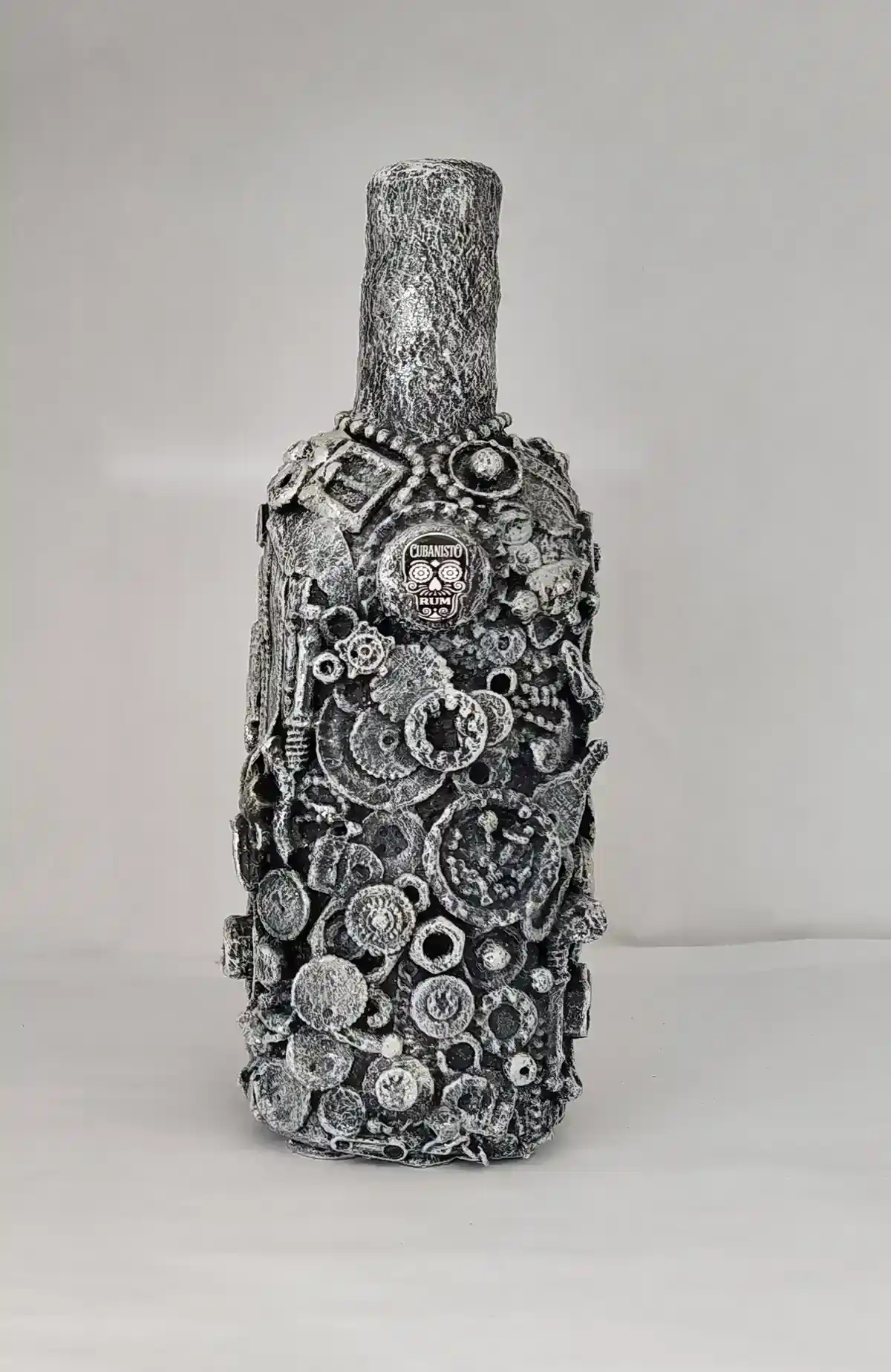 Bottle-O-Rum, a mixed media bottle covered with detritus of glass shards, small plastics and mixed metal pieces