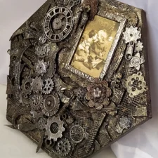 A Moment in Time Mixed media artwork featuring a sepia photograph of a young boy leaning in to kiss a giggling girl, beside a small clock frozen at 10:05 p.m., surrounded by textured layers of paper, cogs, and found objects evoking themes of memory and time.