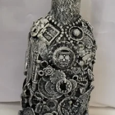 Bottle-0-Rum, a mixed media bottle made covered with detritus of glass shards, small plastics and mixed metal pieces